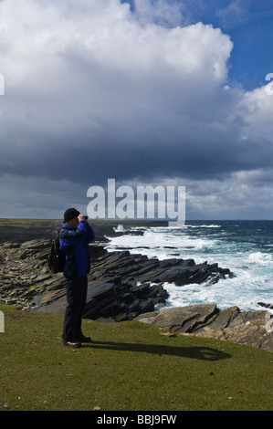 dh Bay of Ryasgeo NORTH RONALDSAY ORKNEY Birdwatcher looking out to sea and rocky coastline birdwatching binoculars