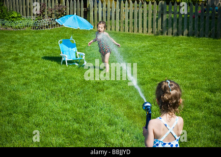 Child suffering a direct hit from a spraying water hose in backyard Stock Photo