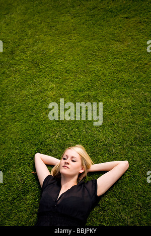 A young woman lies on the grass sunbathing, relaxing, thinking or just resting in the warm sun. Stock Photo