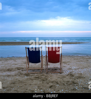 Two wooden deckchairs on the beach in front of the sea at sunset / dusk Stock Photo