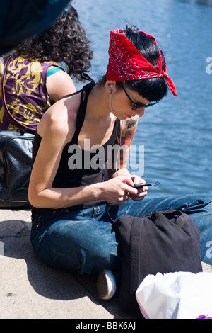 Camden Lock Village Market , pretty young teenage girl with tattooed arm , red head scarf & halter top sits by canal with ipod Stock Photo