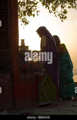 Indian women praying and making offering  under a sacred tree, during a morning ritual. Assi bathing ghat on the river Ganges. Stock Photo
