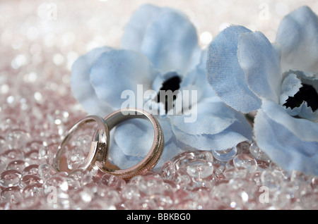 An engagement and a wedding ring next to two light baby blue artificial flowers to be used on the wedding day Stock Photo