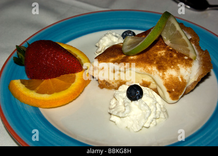 Baked meringue topped slice true key lime pie with sliced lime orange strawberry whipped cream garnish dessert Stock Photo