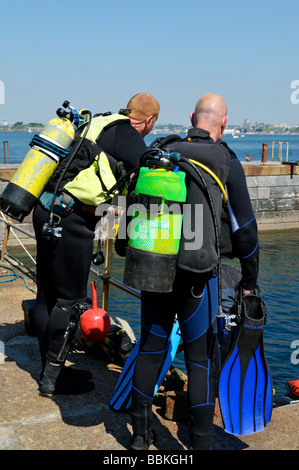 Two scuba divers standing on quayside before with it on before going diving UK Stock Photo