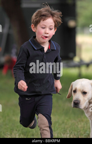 boy running across a meadow watched by a dog Stock Photo