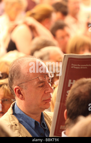 Middle age man male reading a newspaper with his glasses on his head among a crowd at the Hay Festival May 2009 Stock Photo