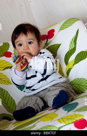 Nine-month-old baby sitting in a chair and biting into a rattle
