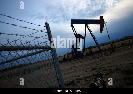 Oil pump jack in evening with fence in Alberta Canada Stock Photo