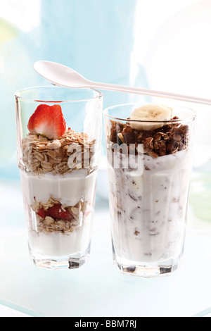 Muesli and chocolate muesli with yoghurt and in a small glass jar, sliced banana, strawberries, yoghurt spoon Stock Photo