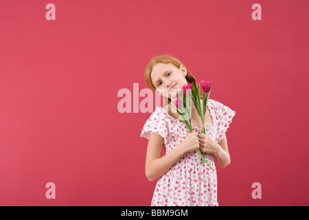 Red-haired girl with braids wearing a summer dress in front of a red backdrop with flowers Stock Photo