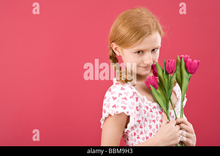 Red-haired girl with braids wearing a summer dress in front of a red backdrop with flowers Stock Photo