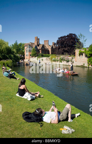 People sitting on the banks of the River Cam at Clare College, Cambridge, watching the punting on a summers day