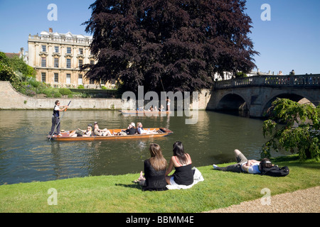 People sitting on the banks of the River Cam at Clare College, Cambridge, watching the punting on a summer day, Clare College, Cambridge University UK