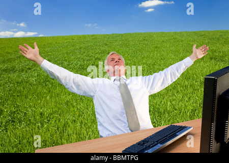 Concept shot showing an older male executive using a computer in a green field with a blue sky complete with fluffy white clouds Stock Photo