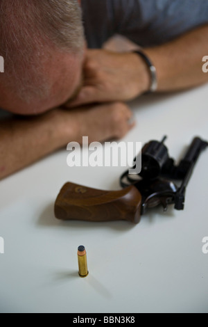 A revolver with one cartrige lying on the table in front of a desperate man