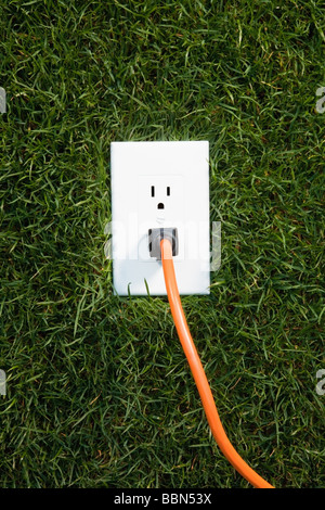 Electrical outlet in grass with extension cord plugged in Stock Photo