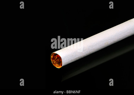 One single white cigarette on a black reflective surface Stock Photo