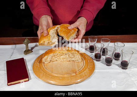 Woman breaking loaf of bread for home church Holy Communion at table set for with bread and wine UK Stock Photo