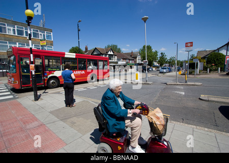 street scene in Chingford London on Essex border with elderly woman on motorbility scooter powered wheelchair, with bus Stock Photo