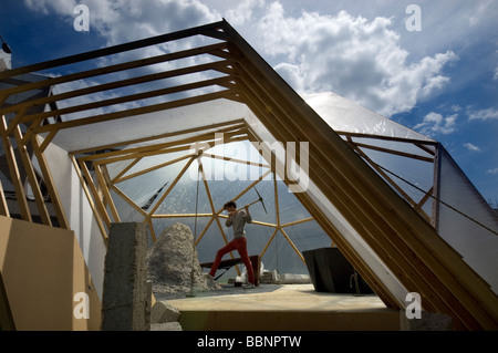 An art student using a pickaxe to shape papier mache rocks of recycled paper  in a geodesic dome for an art show Stock Photo