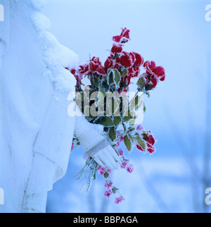Close-up on the hands together by a statue holding a bunch of red flowers. Stock Photo