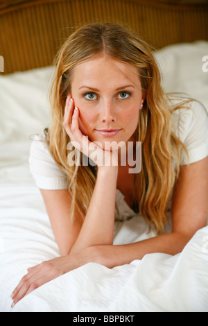 Young Caucasian woman sitting or lying on a white bed thinking. Stock Photo