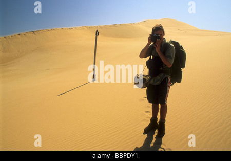 Hiker with camera on sand dunes with route marker in the middle distance in the Alexandria Dune Field, Eastern Cape South Africa Stock Photo