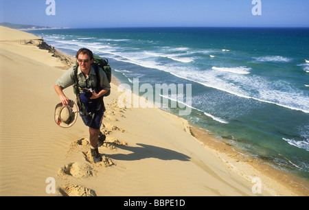 Male caucasian hiker walking up a sand dune in the Alexandria duneveld with the Indian Ocean in the background, South Africa Stock Photo
