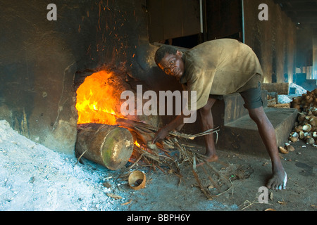 A worker makes a fire under a grill to dry copra Cocos nucifera Quelimane Mozambique Stock Photo