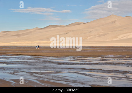 Colorado San Luis Valley Great Sand Dunes National Park Preserve couple crossing Medano Creek to hike on dunes Stock Photo