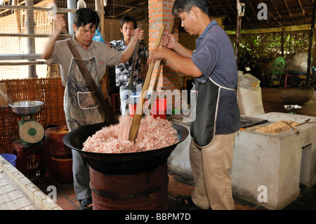 Two men with large wooden spoons stirring in a bowl while preparing puffed rice sweets, confectionery factory, Vinh Long, Mekon Stock Photo