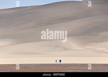 Colorado San Luis Valley Great Sand Dunes National Park Preserve couple crossing Medano Creek to hike on dunes Stock Photo
