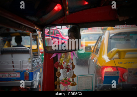 A driver is reflected in the rearview mirror of an Auto rickshaw taxi, commonly known as Tuk Tuk in Bangkok Thailand Stock Photo