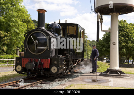 Steam Engine 'Earl' filling up with water at station platform water tower on working narrow gauge railway tourist attraction Stock Photo