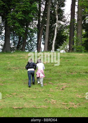 Two girls running up grassy hill Stock Photo