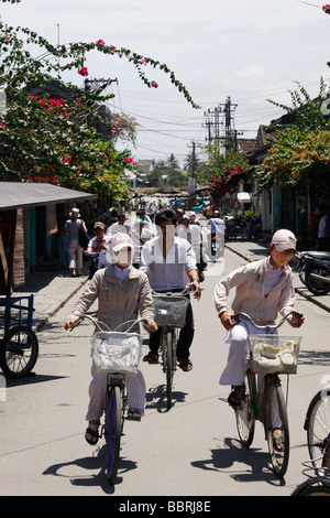 [School girls] riding bikes wearing traditional white 'ao dai' uniform and 'face masks', 'Hoi An', Vietnam Stock Photo