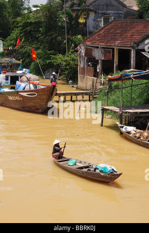 Vietnamese man rowing small wooden [fishing boat] on [dirty brown] water of 'Thu Bon' River, 'Hoi An', Vietnam Stock Photo