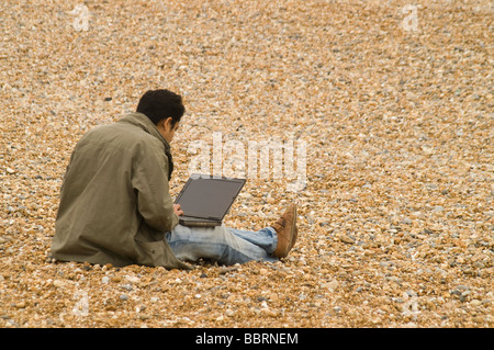 Young male working on a laptop on a pebble beach Stock Photo