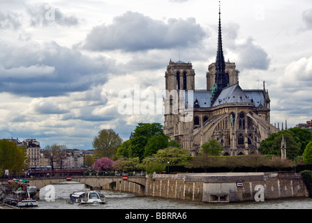 France Paris Notre Dame gothic cathedral catholic church Seine river water ship cloudy overcast sky trees island plant flowering Stock Photo