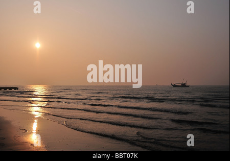 Red sunrise shining on a beach lapped by gentle waves from a calm Adriatic Sea with a fishing boat at Lido di Jesolo, Italy Stock Photo