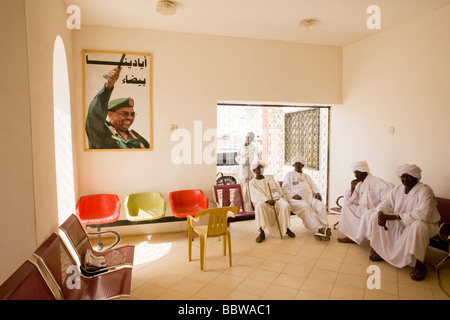 Darfurian men waits beneath imposing portrait of Sudanese President in Al Fashir airport, Omar Hassan Ahmad al-Bashir Stock Photo