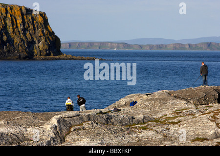 men sea fishing off dangerous rocks on the north antrim coast near ballintoy county antrim with rathlin island Stock Photo