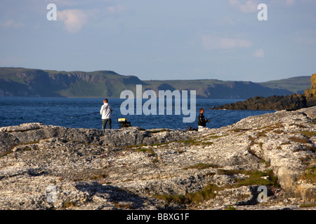 men sea fishing off dangerous rocks on the north antrim coast near ballintoy county antrim with rathlin island Stock Photo