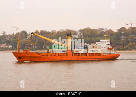 A small to medium size container ship heads out to see along the Elbe, Hamburg Stock Photo