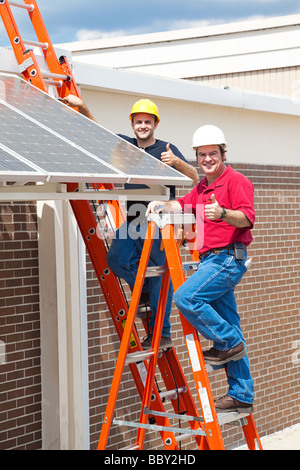 Two workers installing solar panels and giving the thumbs up sign  Stock Photo