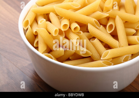 Dry penne rigate in white ceramic bowl on wooden floor Stock Photo