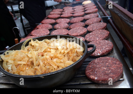 bowl of fried onions and raw hamburgers being cooked on an open grill for sale at a public event county down northern ireland uk Stock Photo