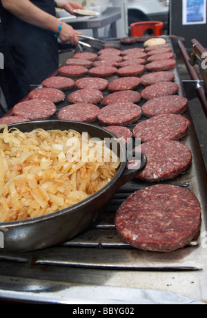 bowl of fried onions and raw hamburgers being cooked on an open grill for sale at a public event county down northern ireland uk Stock Photo