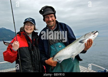Female angler wearing resort baseball cap with fishing guide holding a freshly landed chinook salmon ready to release Stock Photo